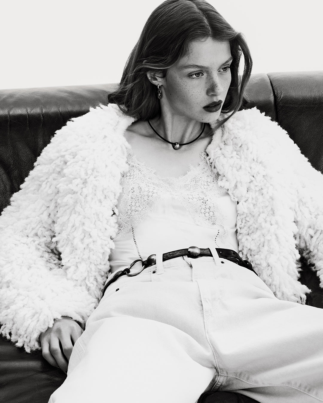 Model in the couch wearing a fluffly jacket and laces top. 