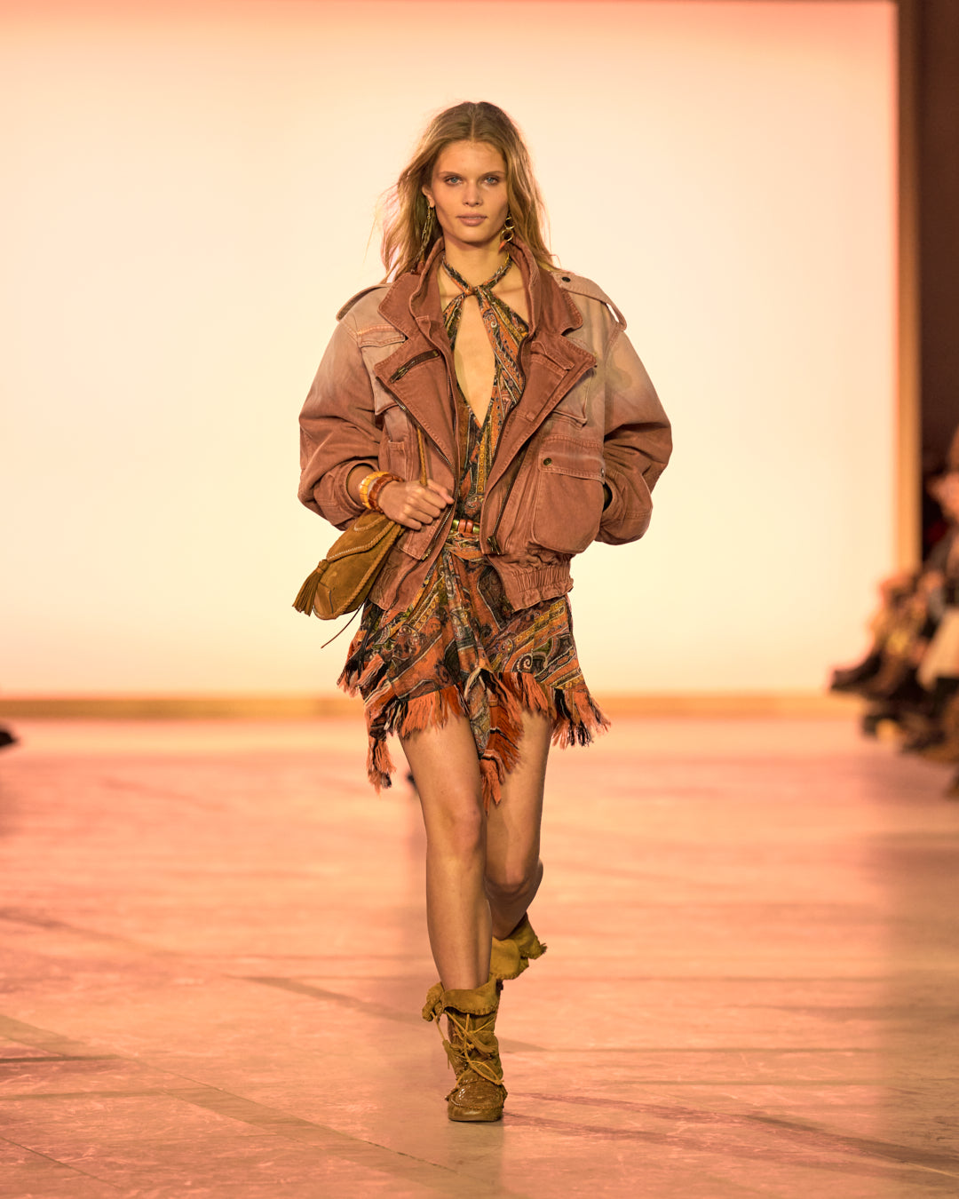 Female model on the catwalk, wearing the Aneli pocket jacket in henna-coloured denim, the Dova draped skirt in orange-printed elastic tulle and the Winki boots in cognac-coloured suede and braided leather.