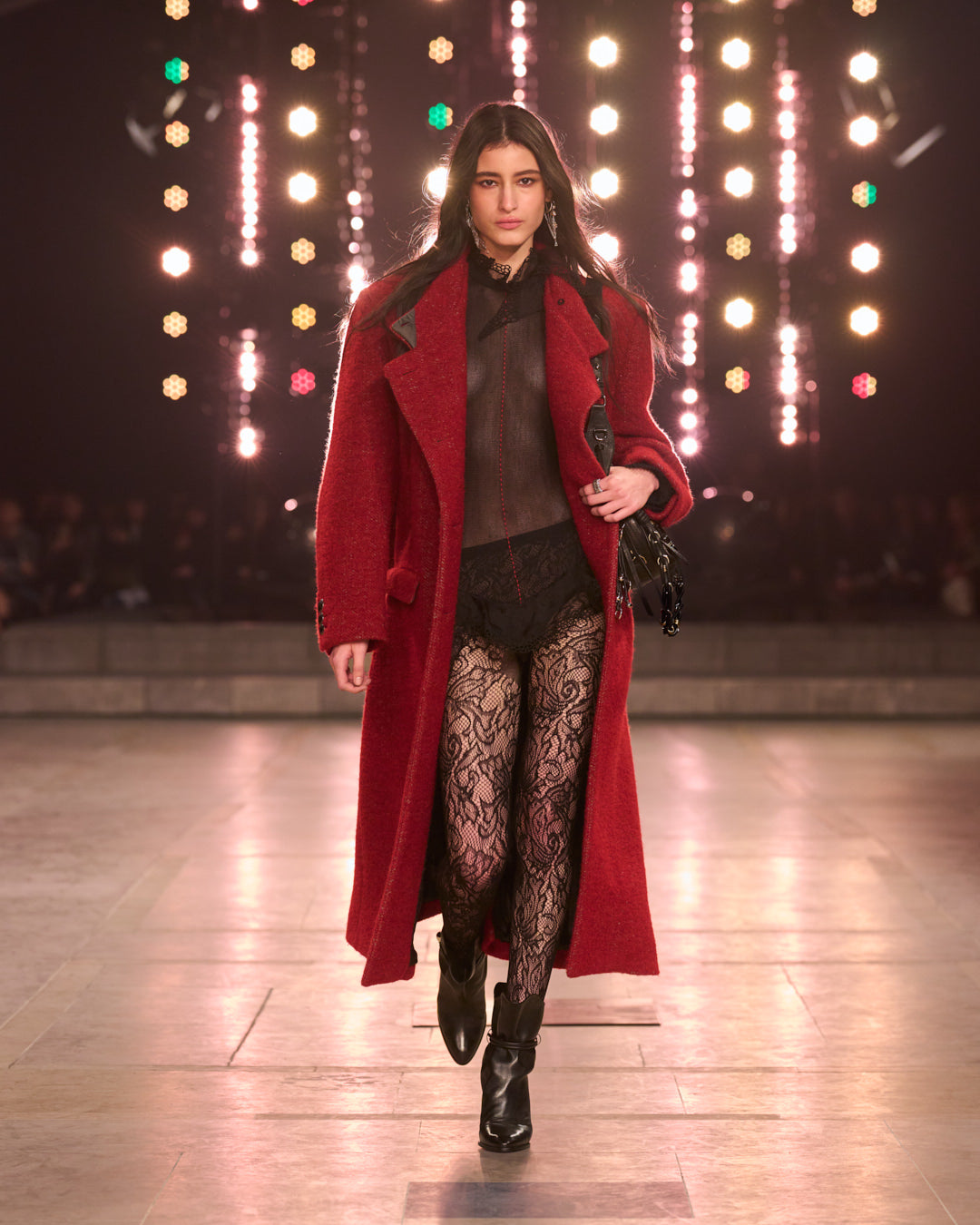 Big lights in the background and in the middle the model wearing a long red coat in wool. 